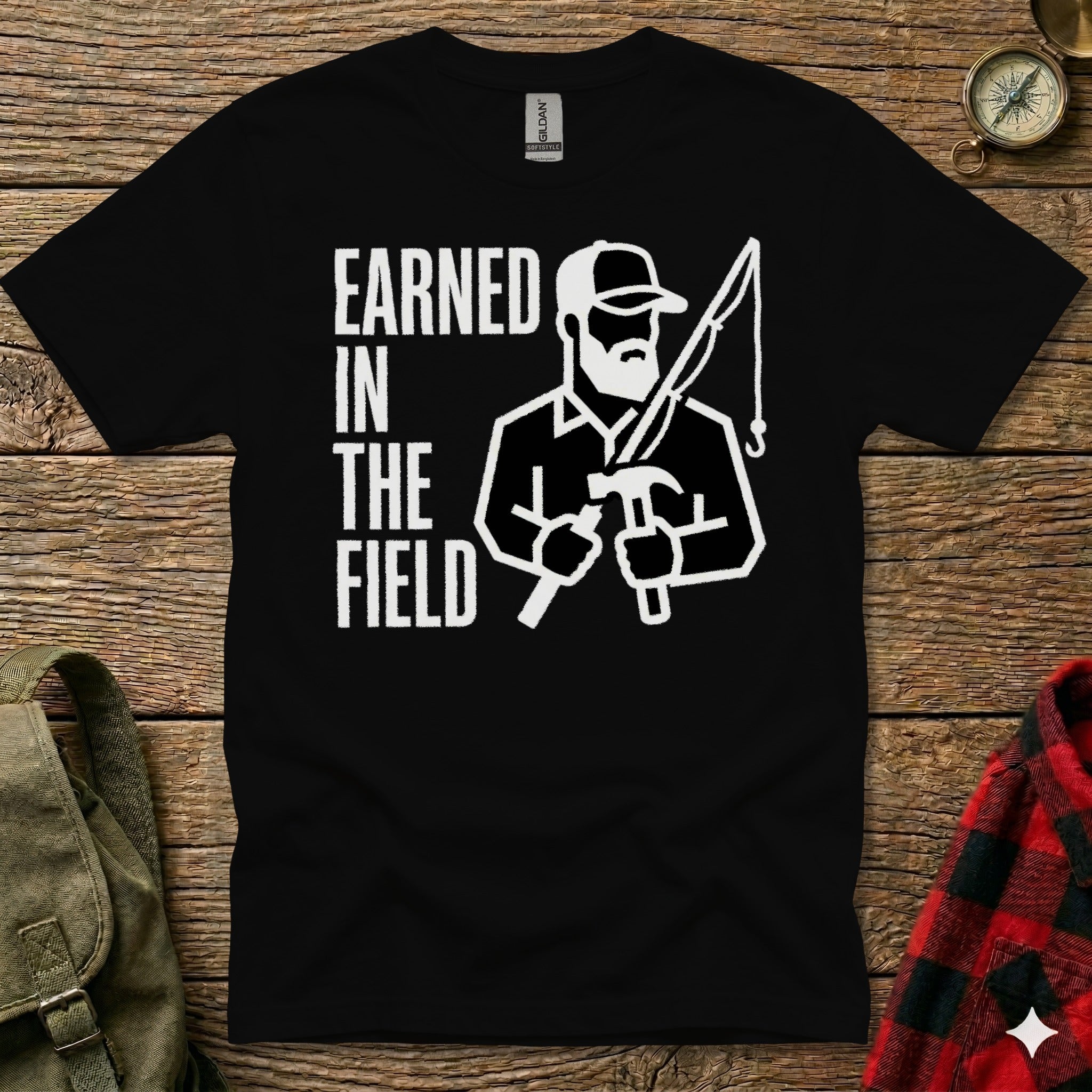 Black t-shirt with "EARNED IN THE FIELD" and graphic of man fishing and hammering.