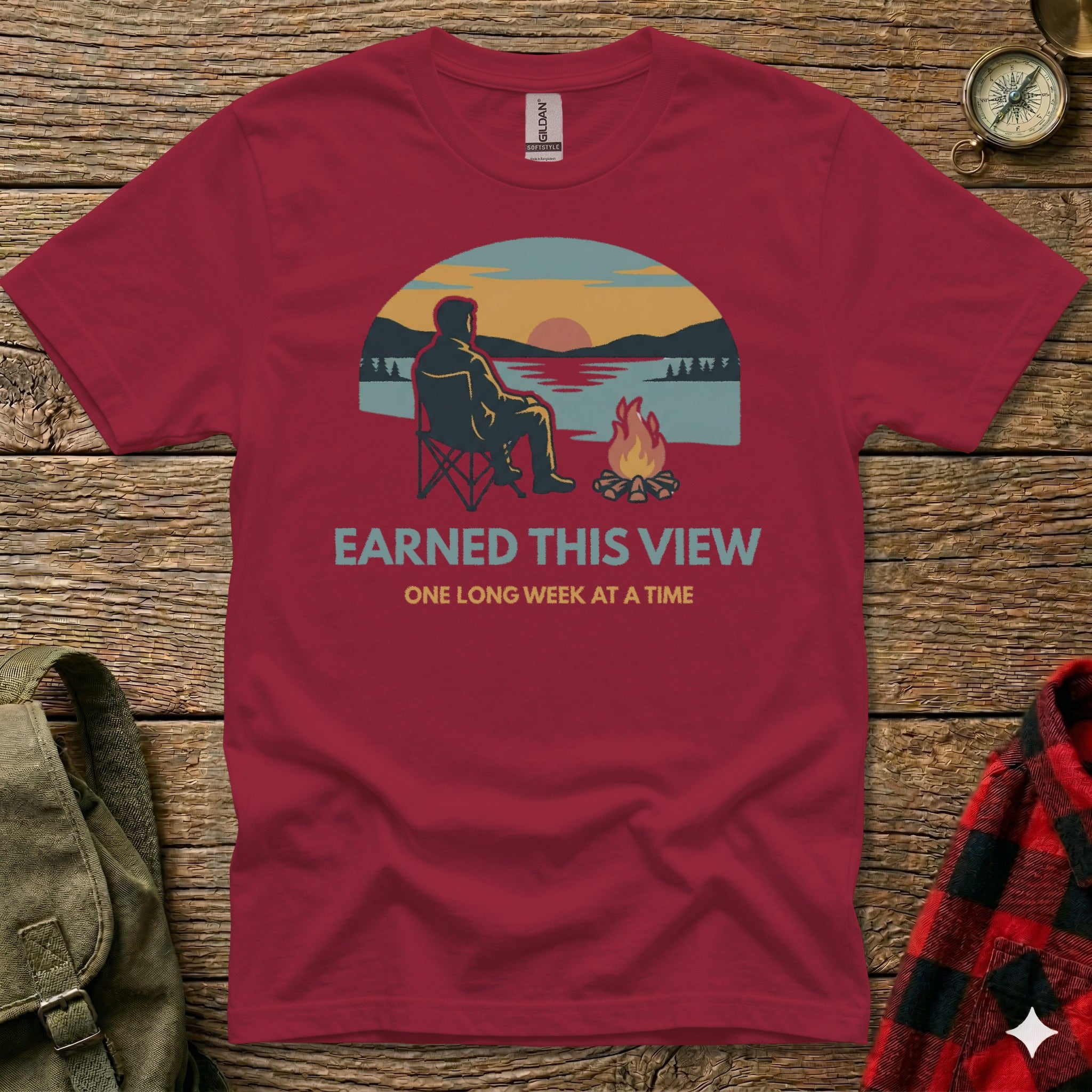 Maroon t-shirt with campfire and sunset graphic, text "EARNED THIS VIEW ONE LONG WEEK AT A TIME".
