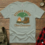 T-shirt with "Stained Hands, Clear Conscience" and boots by campfire.