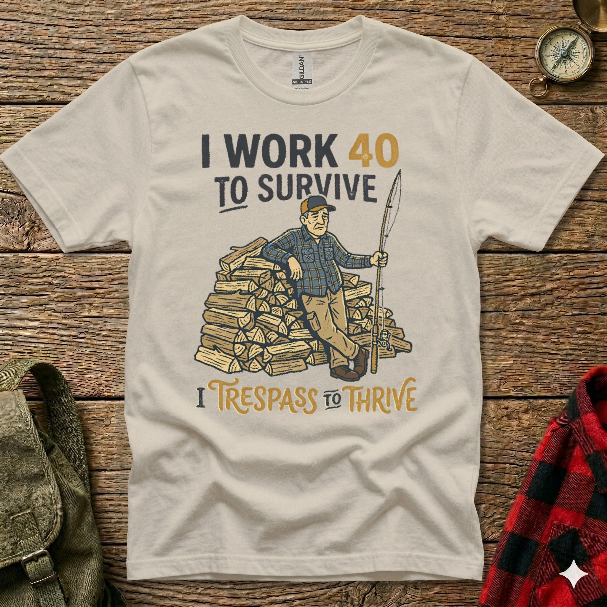 Cream t-shirt with cartoon man leaning on firewood, text "I WORK 40 TO SURVIVE" and "I TRESPASS TO THRIVE".
