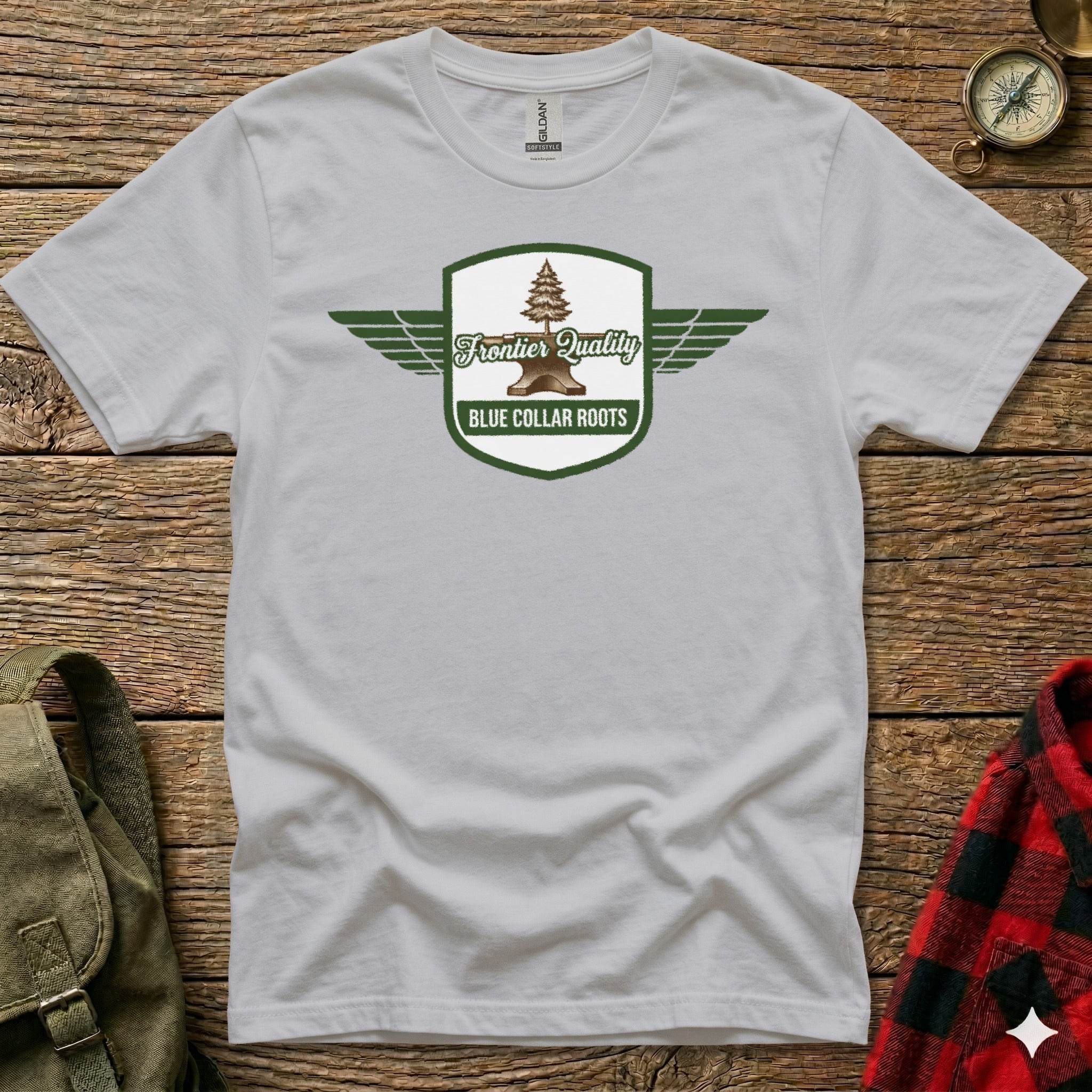 White t-shirt with a green shield logo featuring wings and the text "Frontier Quality Blue Collar Roots".