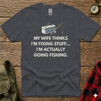 Dark grey t-shirt with white text: "My wife thinks I'm fixing stuff... I'm actually going fishing."