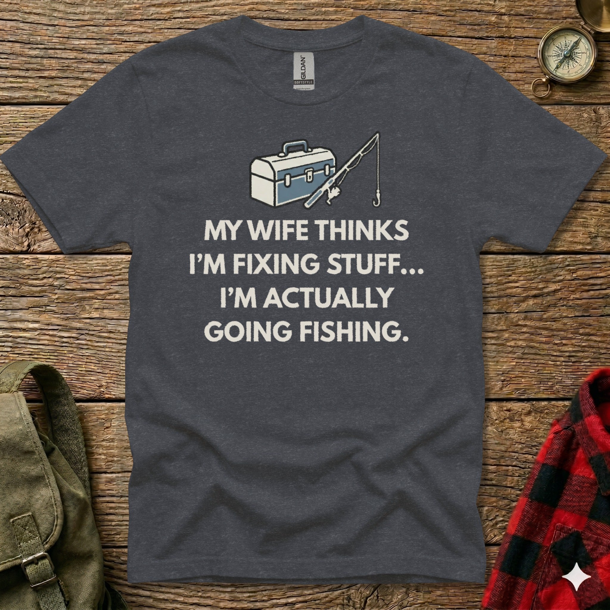 Dark grey t-shirt with white text: "My wife thinks I'm fixing stuff... I'm actually going fishing."