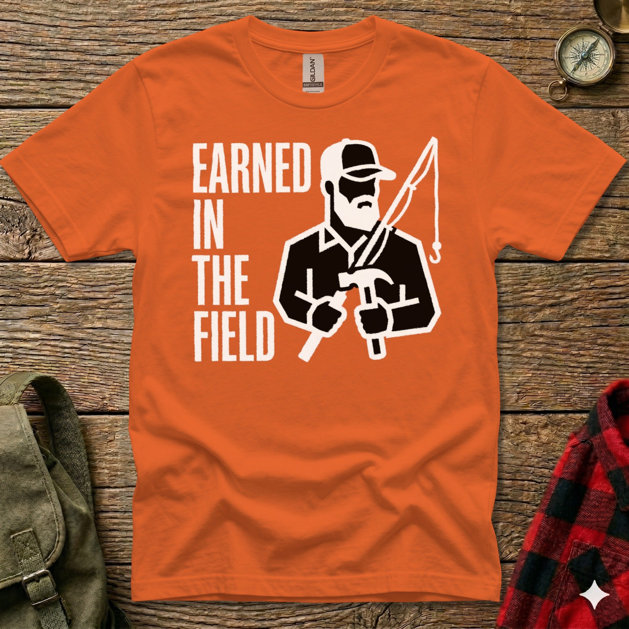 Orange t-shirt with "EARNED IN THE FIELD" and graphic of man fishing and hammering.