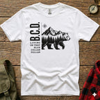 White t-shirt with B.C.D. text and a bear walking through a mountain forest.