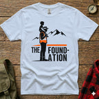 White t-shirt with graphic of man carrying child on shoulders, mountains, and text "The Foundation".