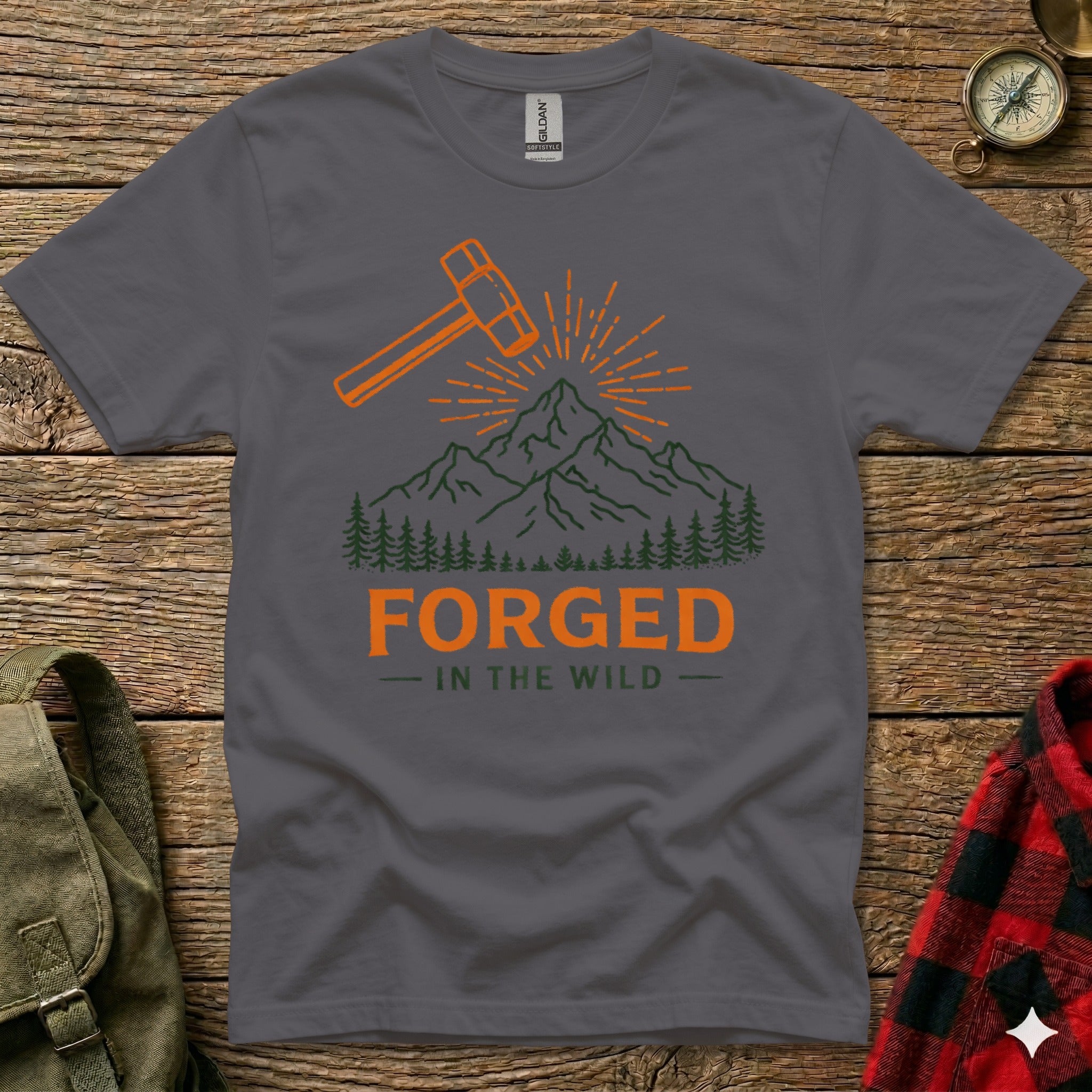 Dark grey t-shirt with orange hammer and mountains graphic, text reads "FORGED IN THE WILD".