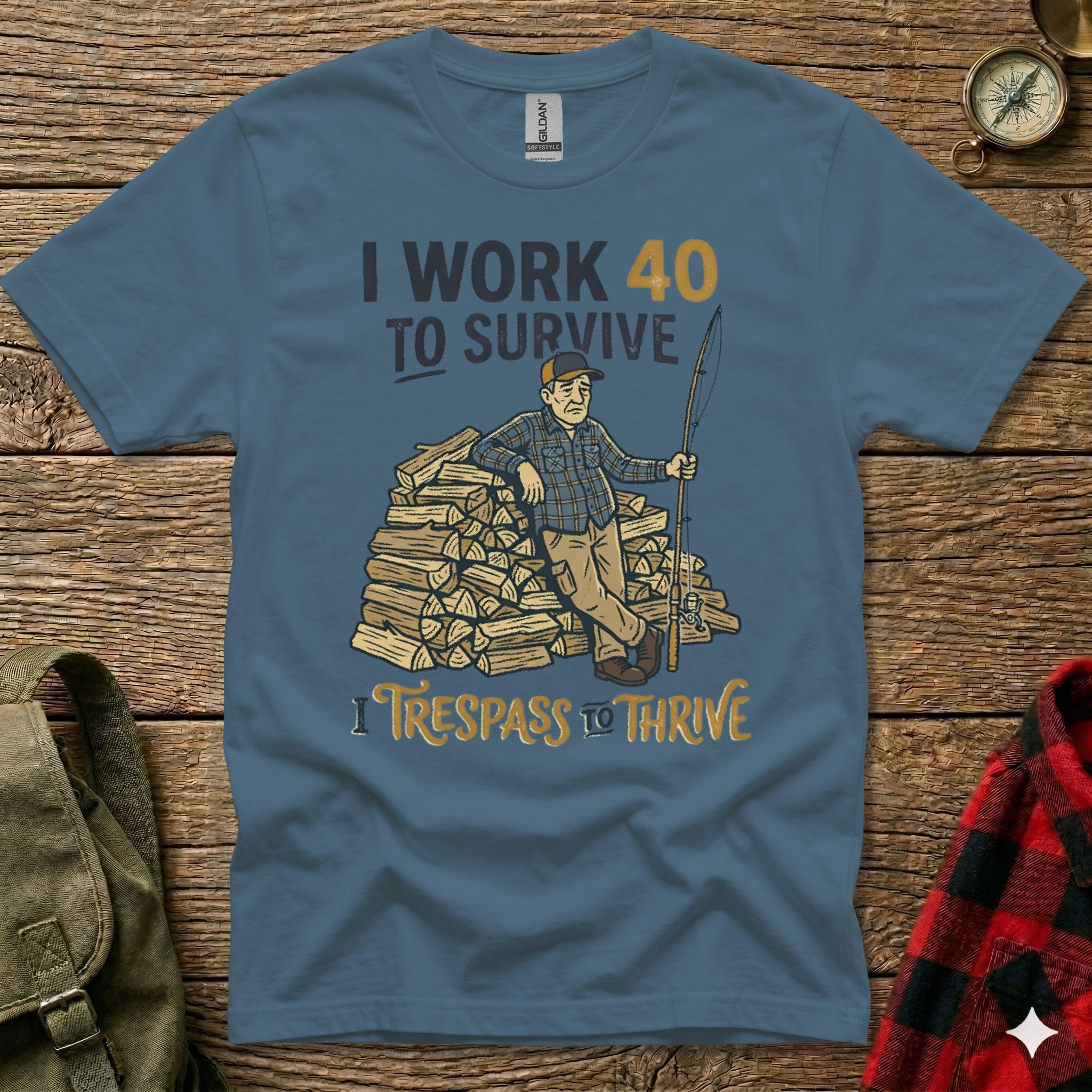 T-shirt with graphic of man fishing next to woodpile, text "I WORK 40 TO SURVIVE" and "I TRESPASS TO THRIVE".