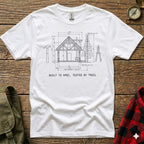 White t-shirt with a diagram of a log cabin and text "BUILT TO SPEC, TESTED BY TRAIL".