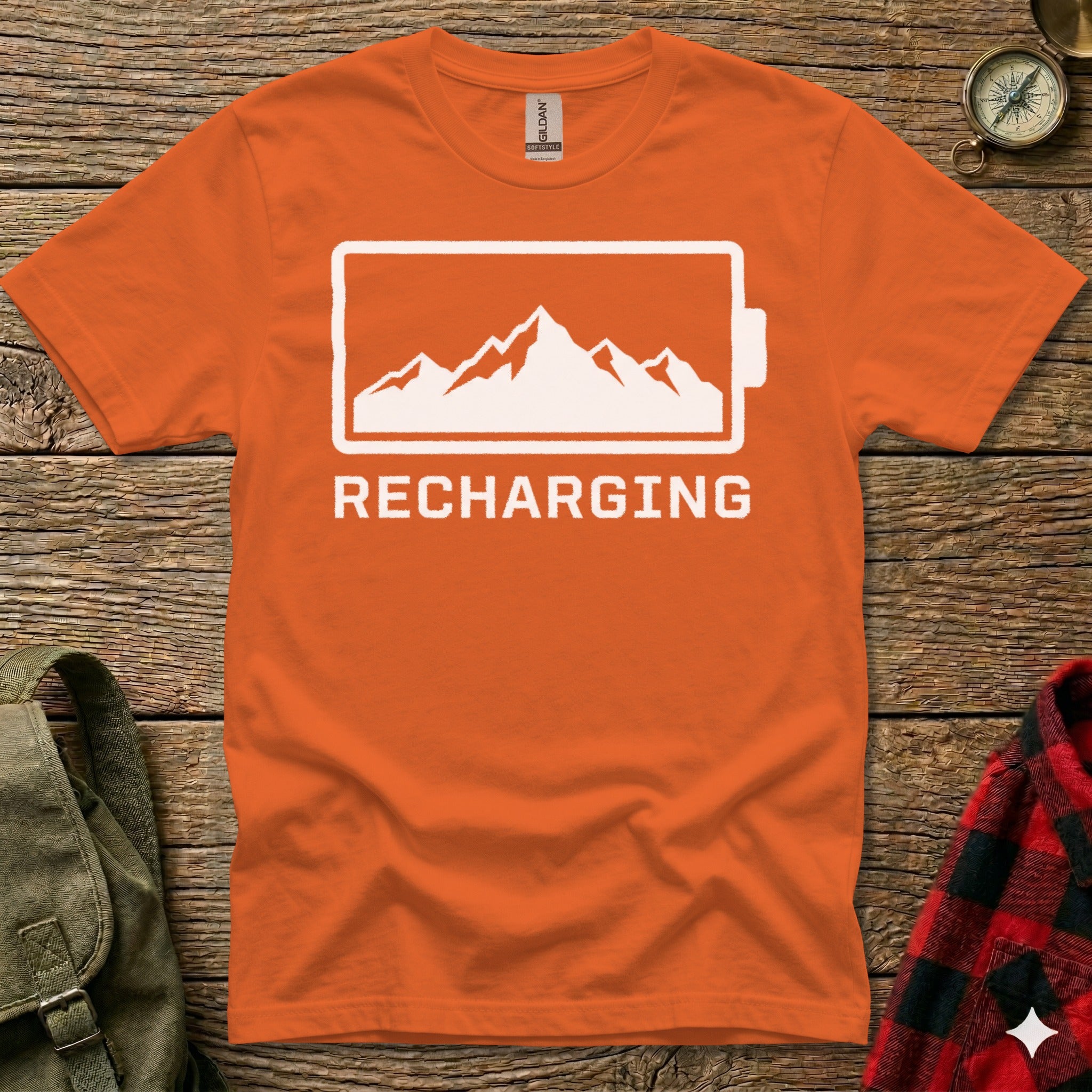 Orange t-shirt with white battery icon and mountain graphic, text "RECHARGING".