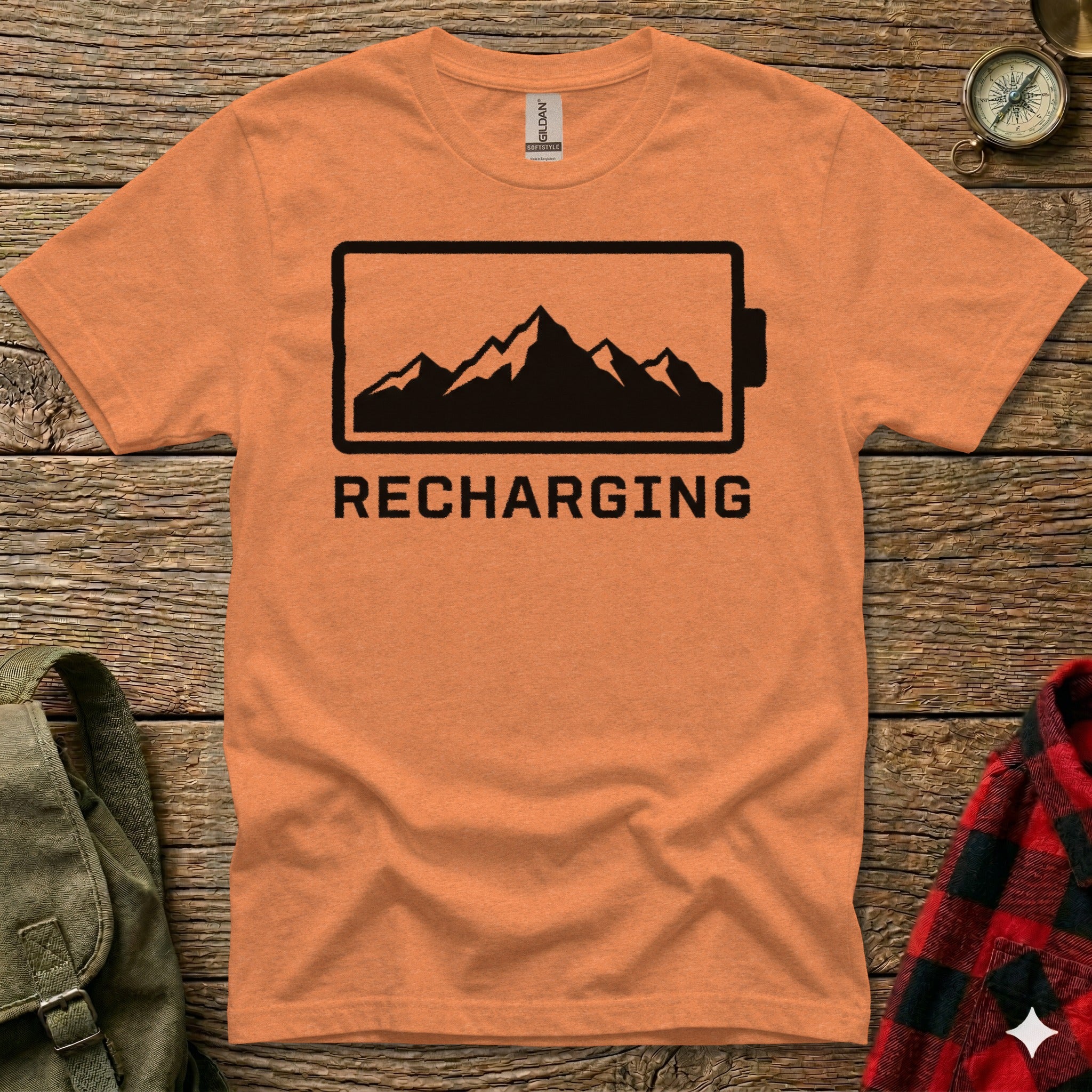 Orange t-shirt with black battery icon and "RECHARGING" text featuring mountains.