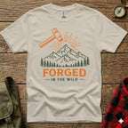Cream t-shirt with orange hammer, mountains, and "Forged in the Wild" text.