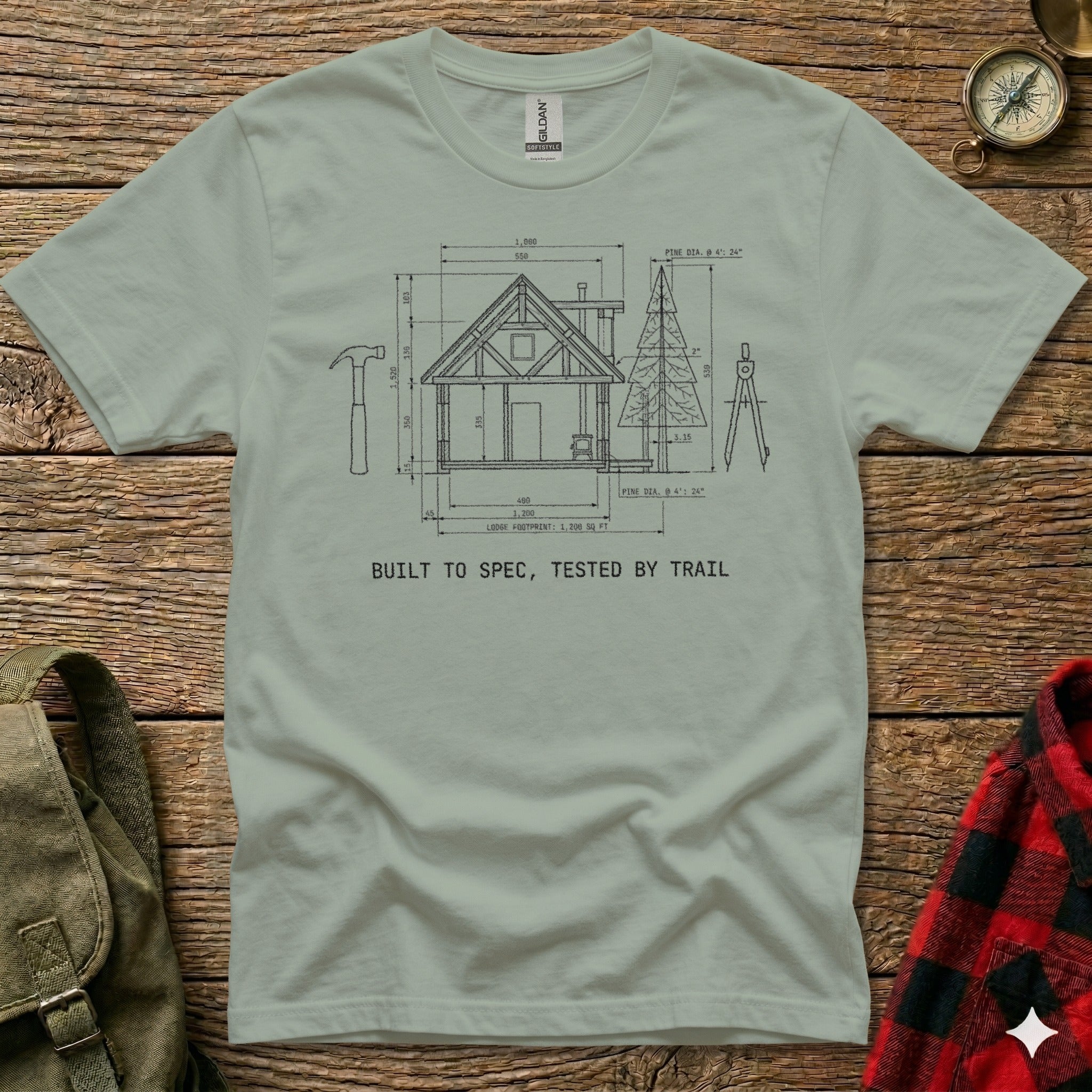 T-shirt with blueprint diagram of a lodge and text "BUILT TO SPEC, TESTED BY TRAIL".
