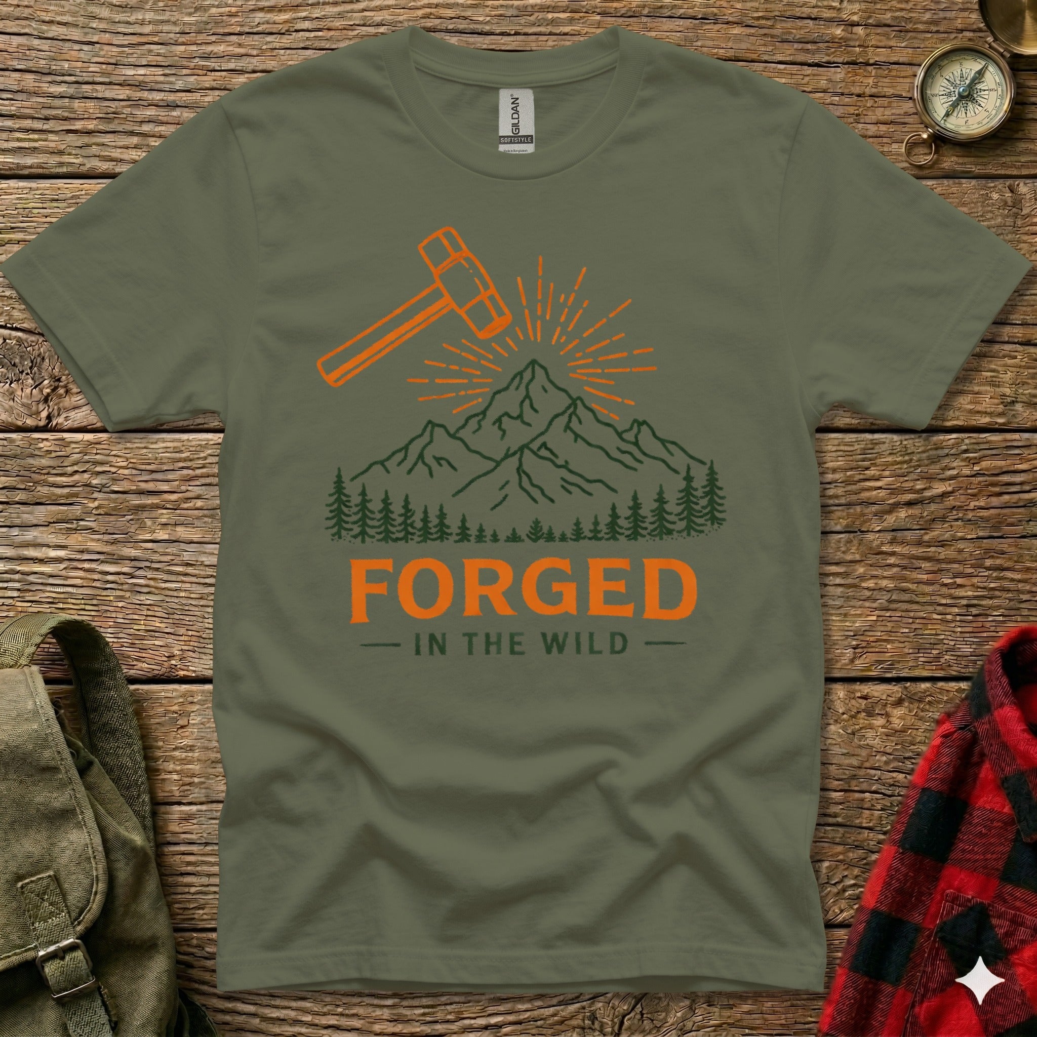 Green t-shirt with orange hammer, sunburst, and mountain graphic, text "FORGED - IN THE WILD".