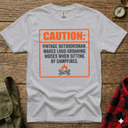 White t-shirt with orange graphic: "CAUTION: VINTAGE OUTDOORSMAN. MAKES LOUD GROANING NOISES WHEN SITTING BY CAMPFIRES."