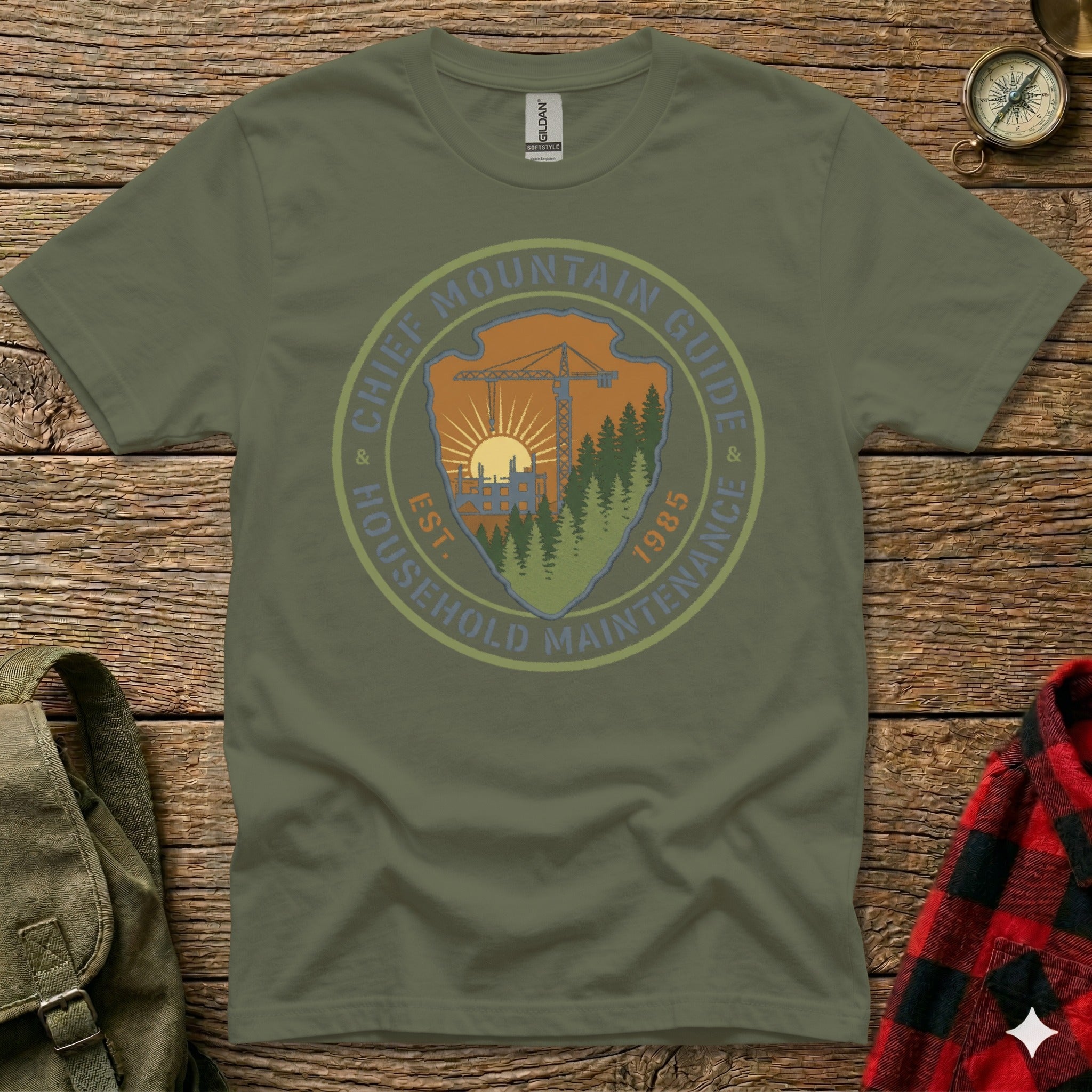 Olive green t-shirt with circular "Chief Mountain Guide Household Maintenance" graphic.