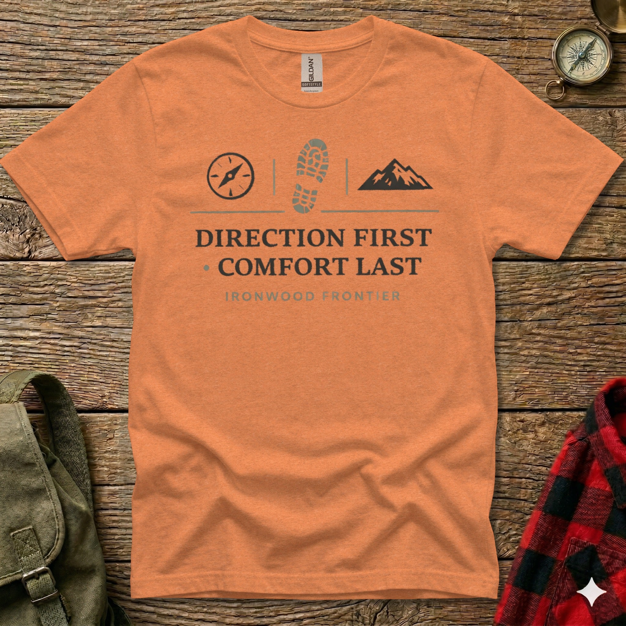 Orange t-shirt with compass, boot print, and mountain graphic, reading "DIRECTION FIRST COMFORT LAST".