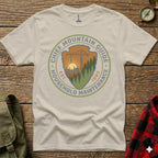 Cream t-shirt with "Chief Mountain Guide Household Maintenance Est. 1985" circular logo.