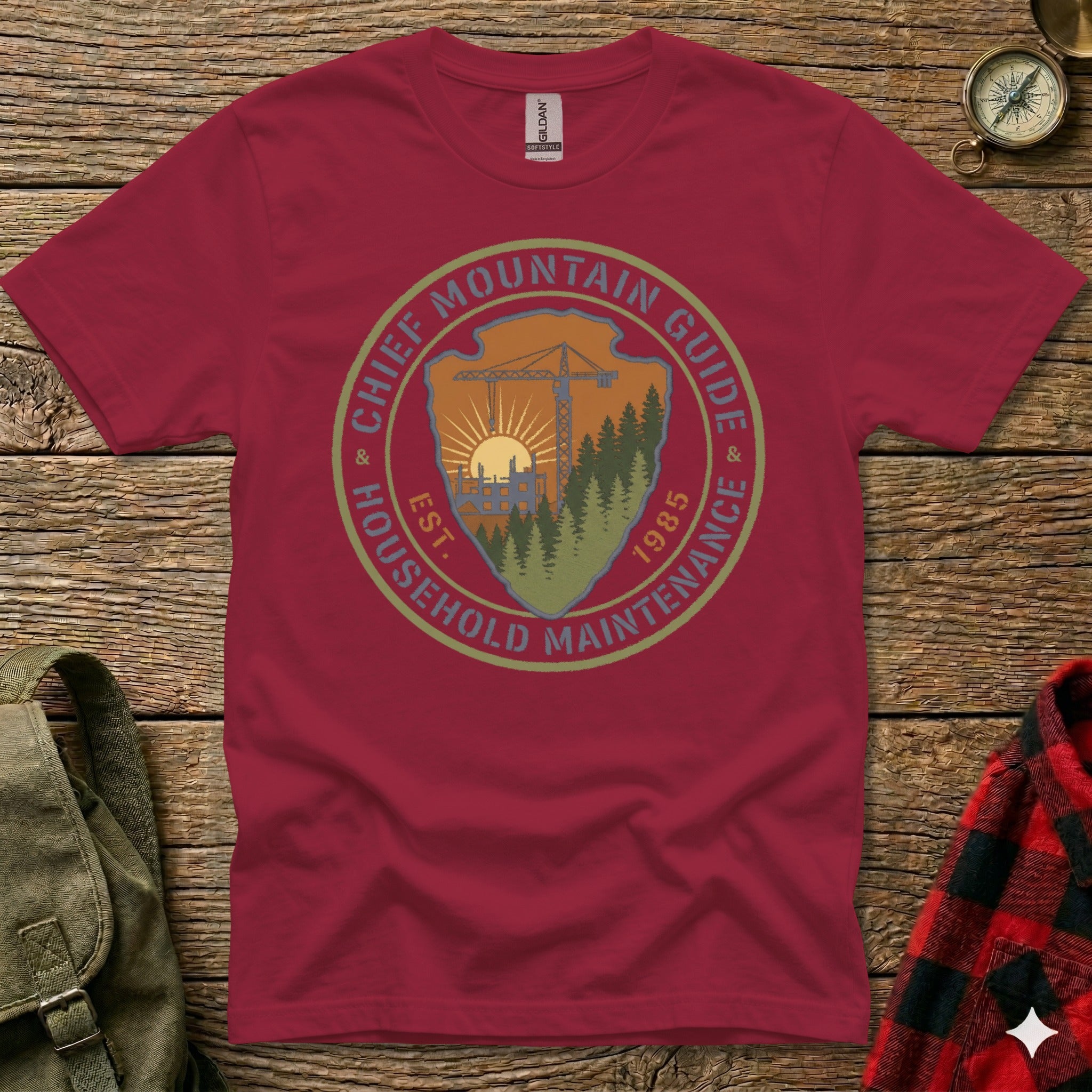 Crimson t-shirt with circular "Chief Mountain Guide Household Maintenance" logo and "Est. 1985" text.