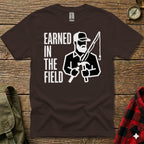 Brown t-shirt with "EARNED IN THE FIELD" and a graphic of a man fishing and hammering.